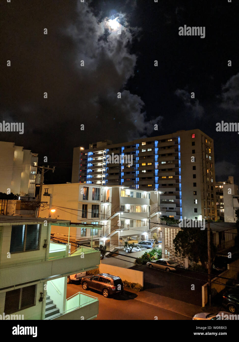 Full moon behind the clouds in Makiki, and Honolulu Cityscape high up during the evening with houses and modern highrises, and other small buildings. Stock Photo