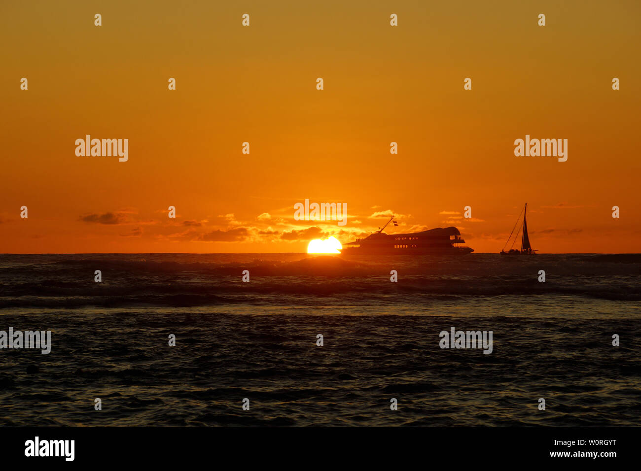 Sunset over the ocean with light reflecting on ocean waves moving with boats on the water in the distance off Waikiki with clouds on Oahu, Hawaii. Stock Photo