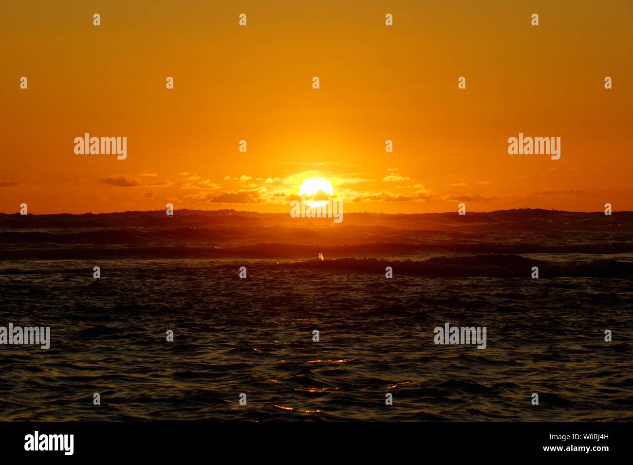 Dramatic lighting the sky and ocean during sunsets with light reflecting on ocean waves moving off Waikiki with clouds on Oahu, Hawaii. Stock Photo