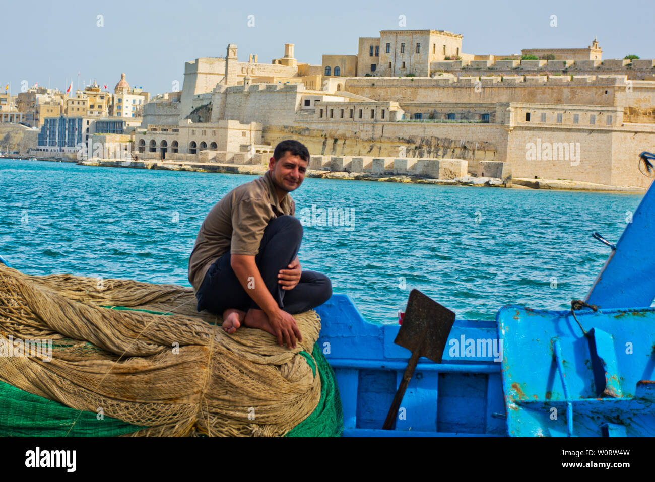 Fisherman sitting on fishing nets with view across the Grand Harbour in Valletta, Malta Stock Photo