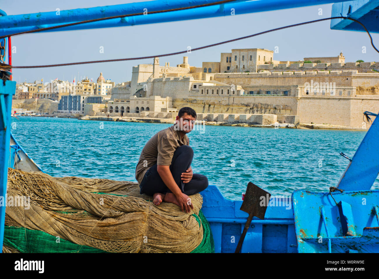 Fisherman sitting on fishing nets with view across the Grand Harbour in Valletta, Malta Stock Photo