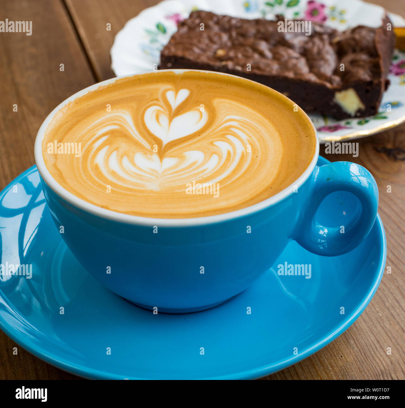 Flat white in bright blue cup with chocolate nut brownie on a vintage plate in the background Stock Photo