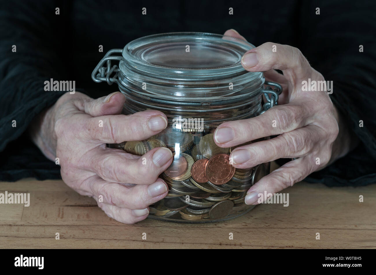 Haende einer alten Frau halten ein Einmachglas mit Kleingeld. Stock Photo
