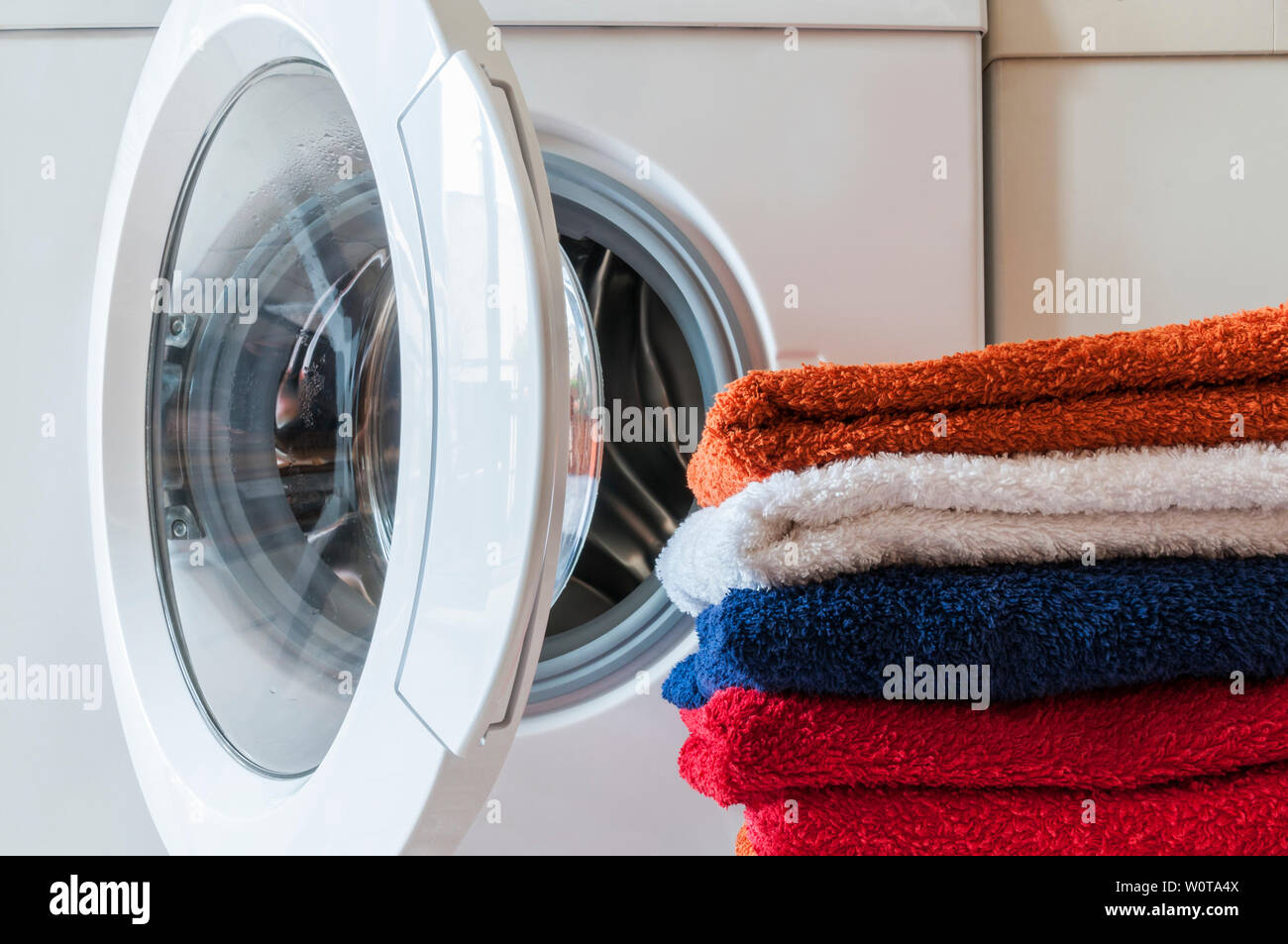 Waschservice, Hausarbeit, Waschmaschine und ein Stapel bunter Handtuecher. Stock Photo