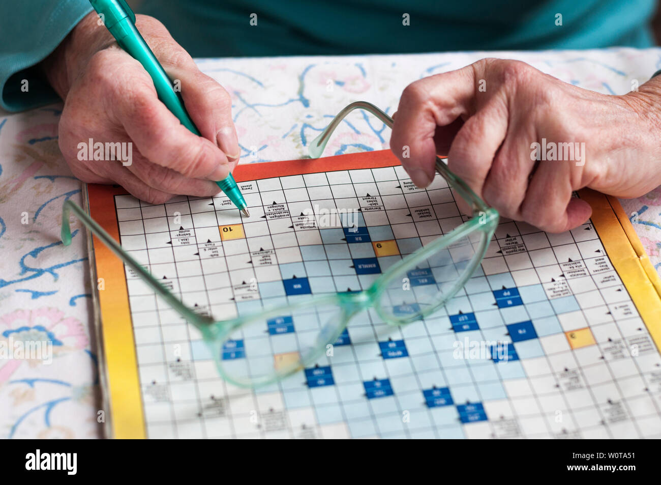 Seniorin sitzt an einem Tisch und loest Kreuzwortraesel. Stock Photo