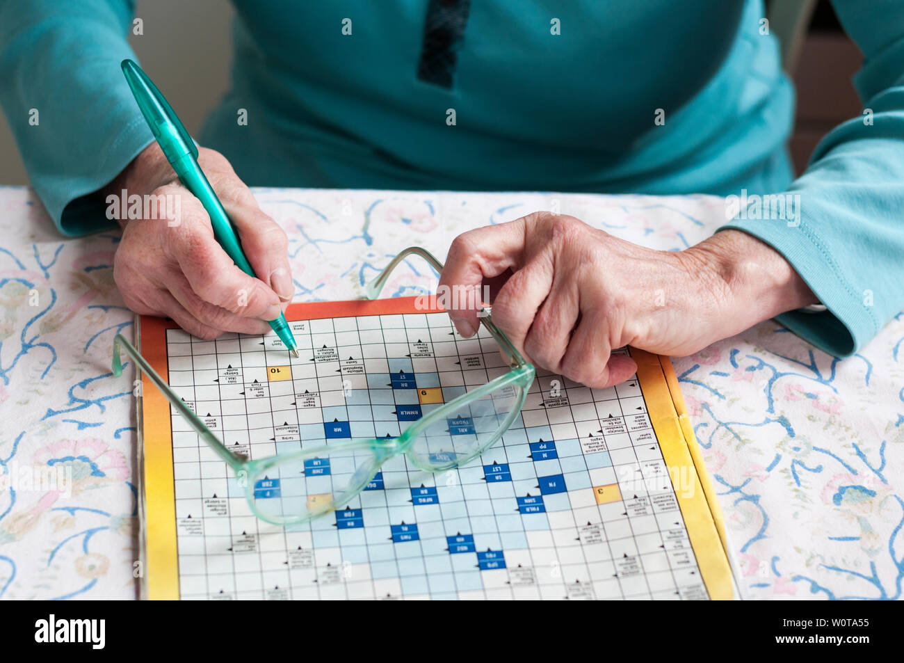 Seniorin sitzt an einem Tisch und loest Kreuzwortraesel. Stock Photo