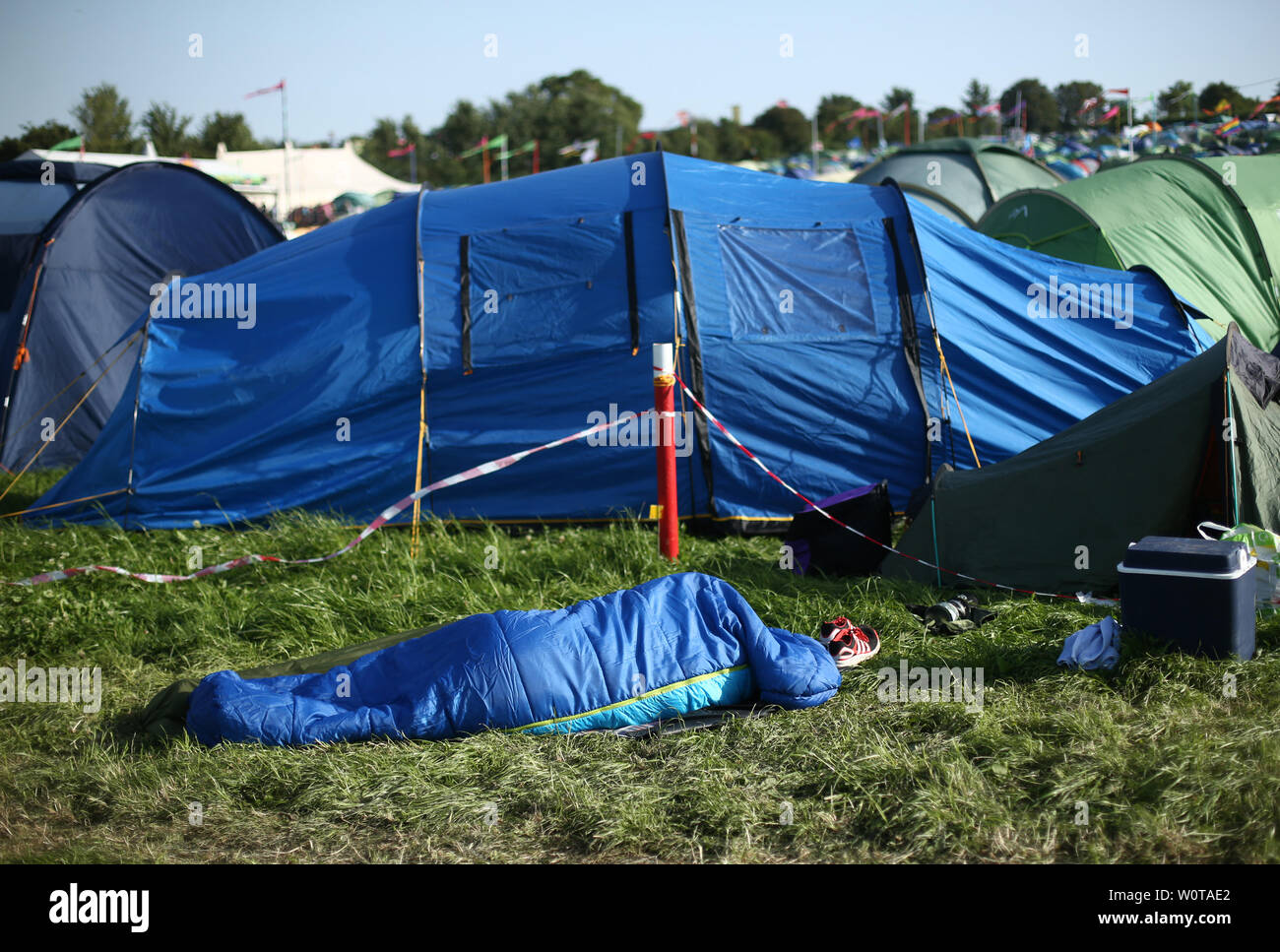 A festivalgoer in a sleeping bag outside a tent on the third day of the