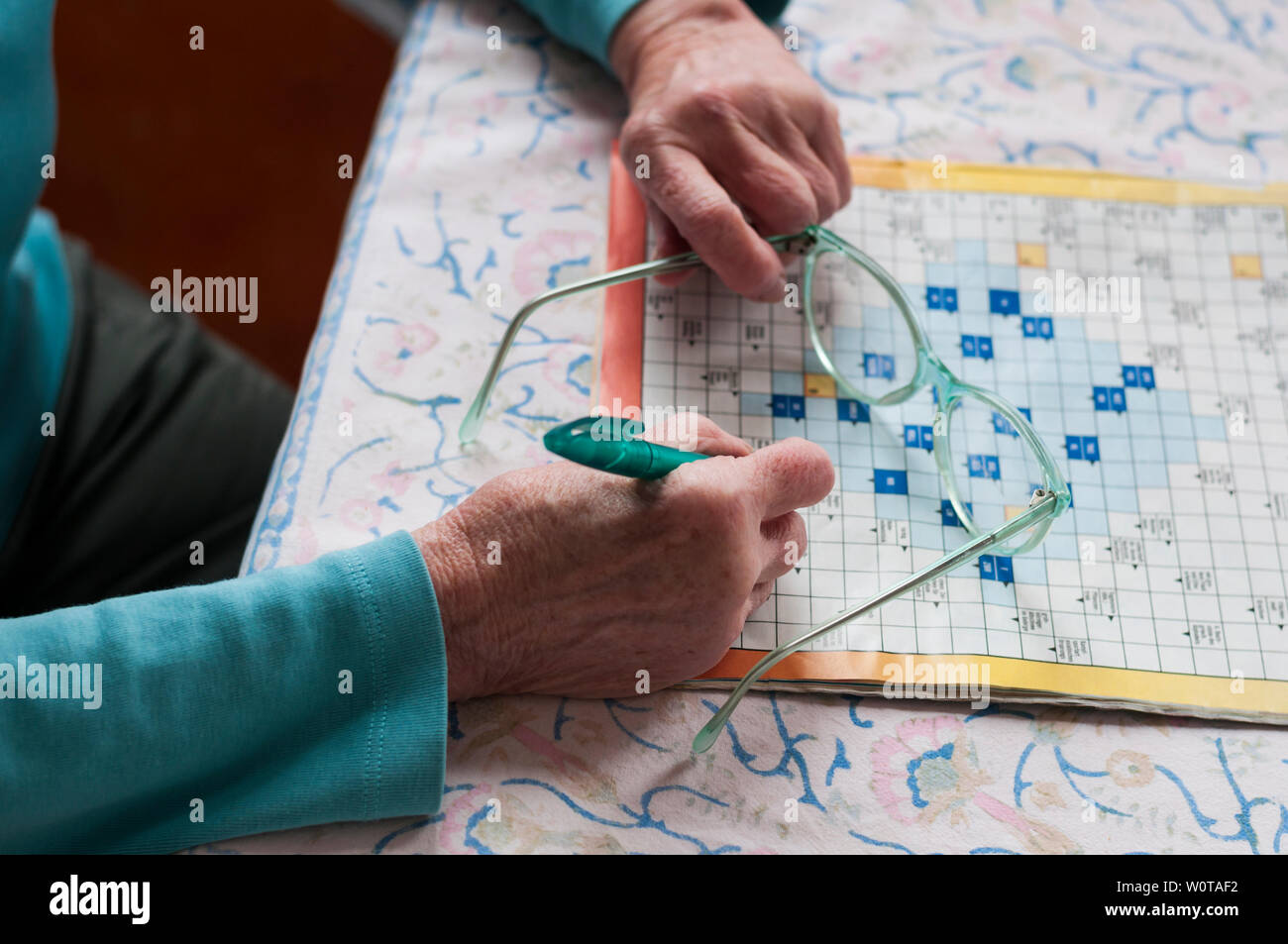 Seniorin sitzt an einem Tisch und loest Kreuzwortraesel. Stock Photo