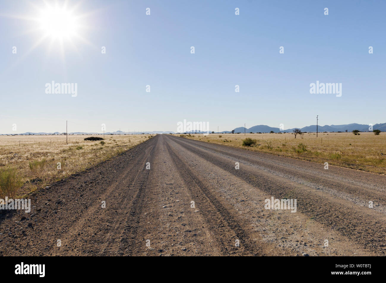 Landschaft mit gerader Strasse bis zum Horizont und Sonne, Namibia, Afrika. Stock Photo