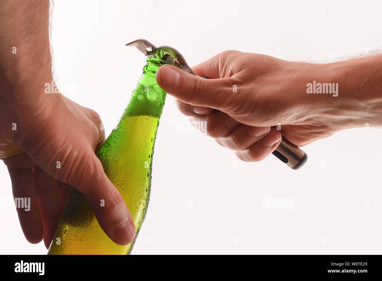 Opening a green glass bottle with a metal bottle opener and white isolated background.  Horizontal composition. Front view. Stock Photo