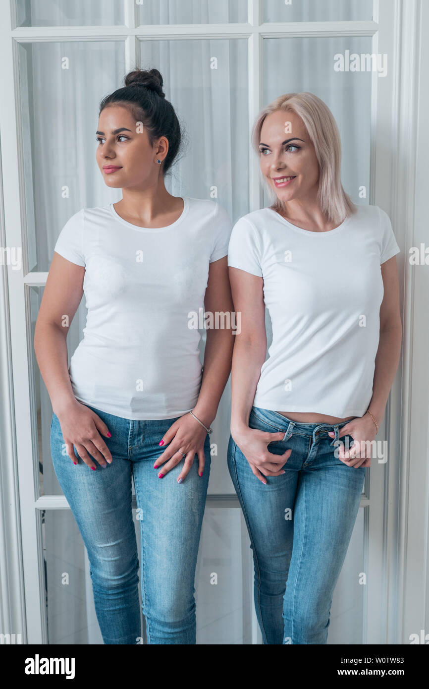 Two beautiful blonde and brunette girls posing in white t-shirts and jeans Stock Photo