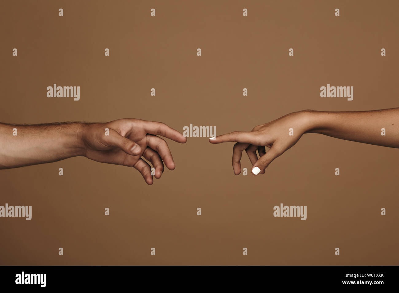 Close up of man and woman hand about to touch with index finger. Couple in love reaching to one another in front of brown background. Stock Photo