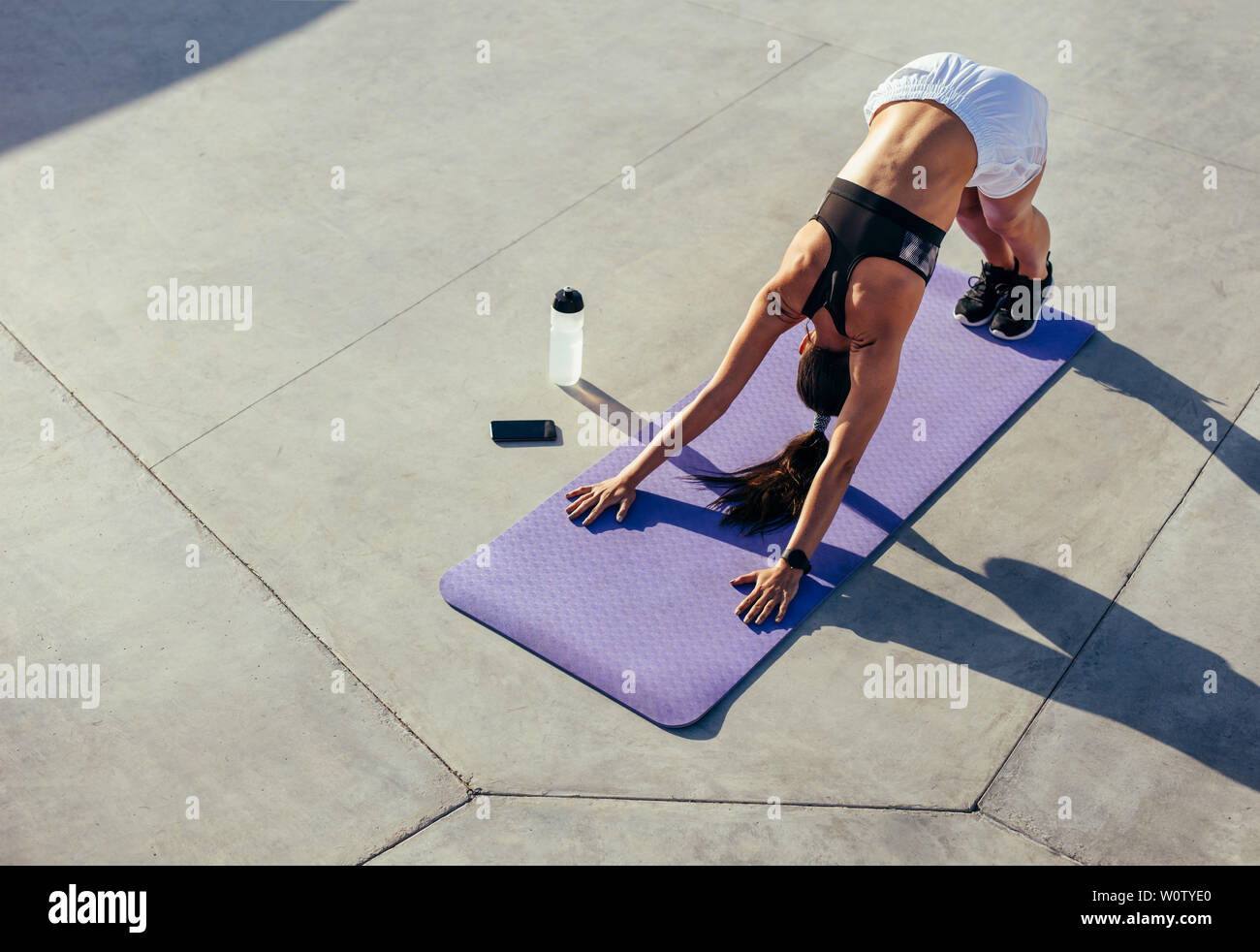Fitness woman practising yoga in morning. Young female in sportswear doing stretching workout outdoors. Downward facing dog yoga pose. Stock Photo