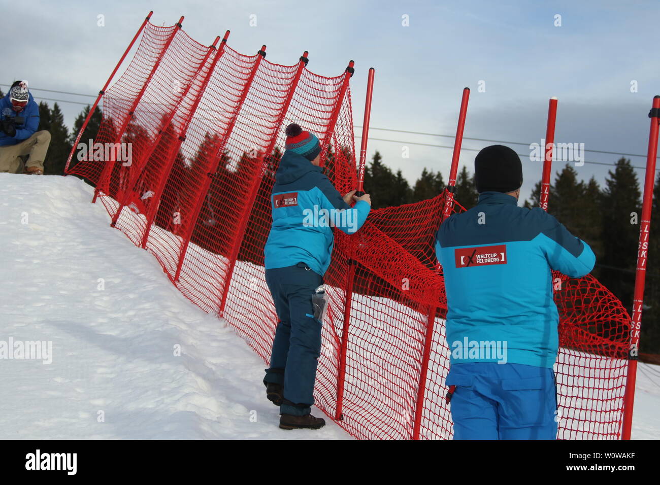 Trotz Sonnenschein, aber teilweise orkanartigen Sturmböen führten zur Absage des FIS-Weltcup im Team Snowboard Cross SBX am Feldberg im Schwarzwald - Der Wind bläst die Fangzäune in Schräglage, die Weltcup-Helfer bauen den Zaun ab. Stock Photo
