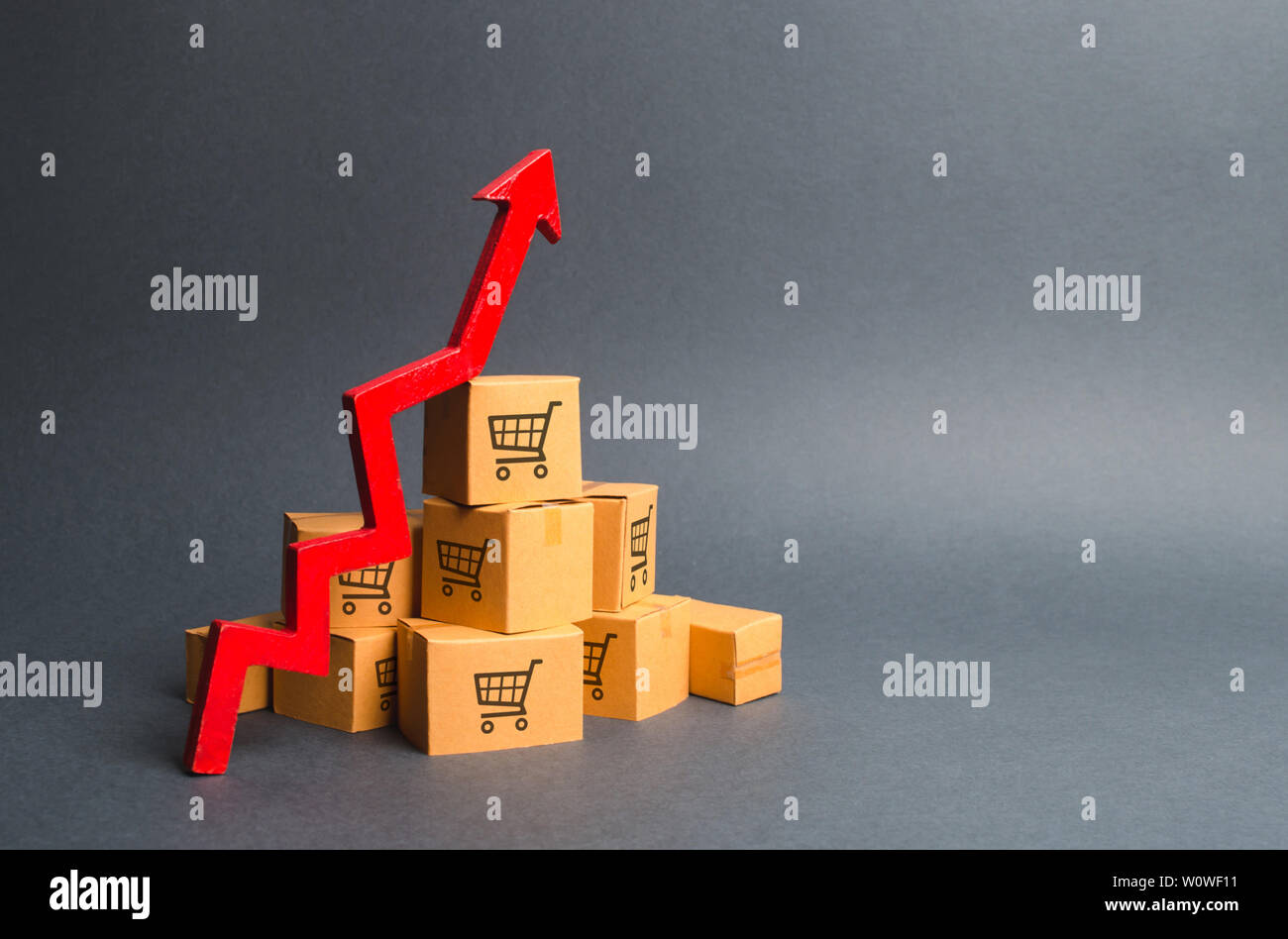 A pile of cardboard boxes with drawing of shopping carts and a red up arrow. The growth rate of production of goods and products, increasing economic Stock Photo