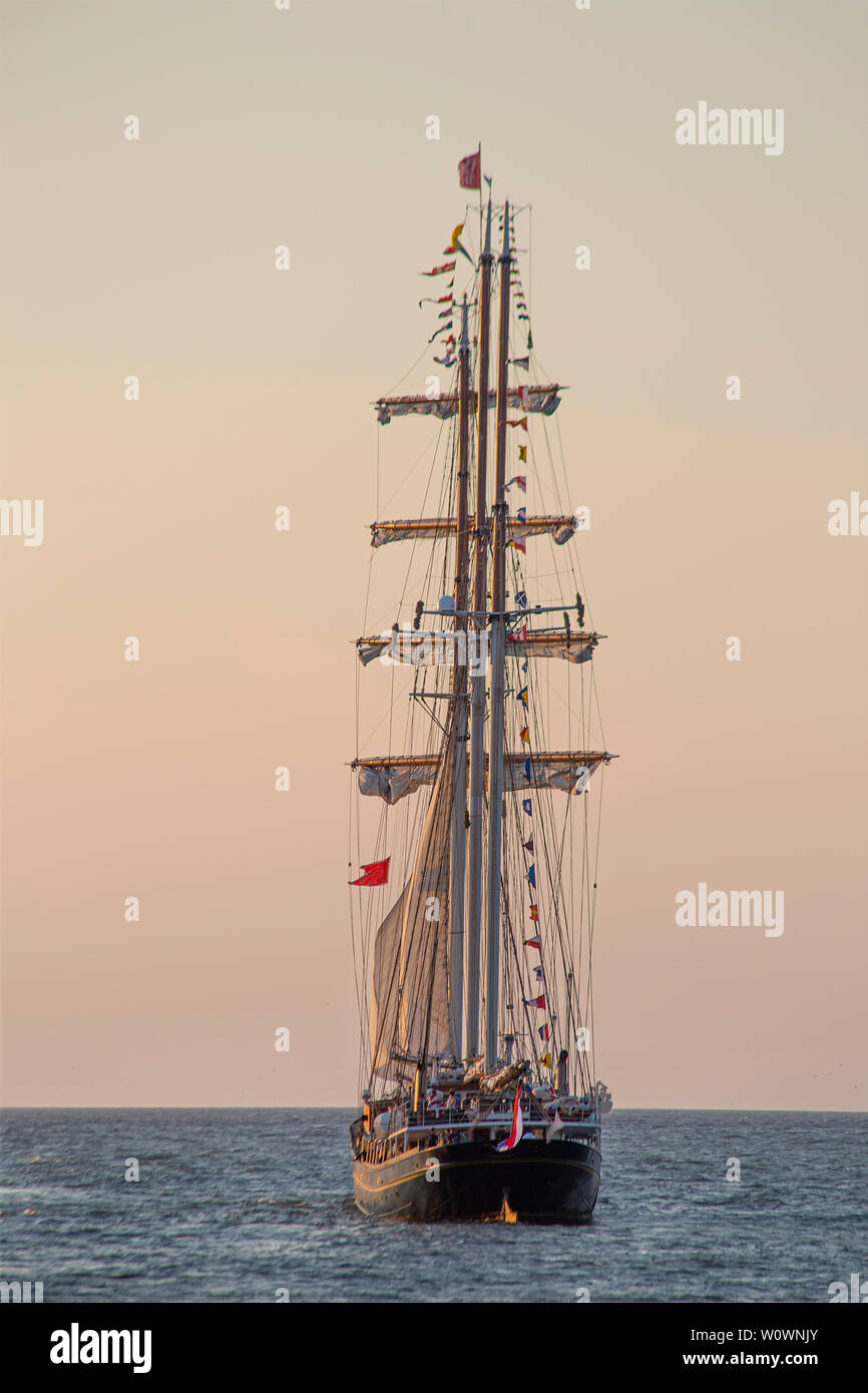 Antique tall ship, vessel leaving the harbor of The Hague, Scheveningen under a warm sunset and golden sky Stock Photo