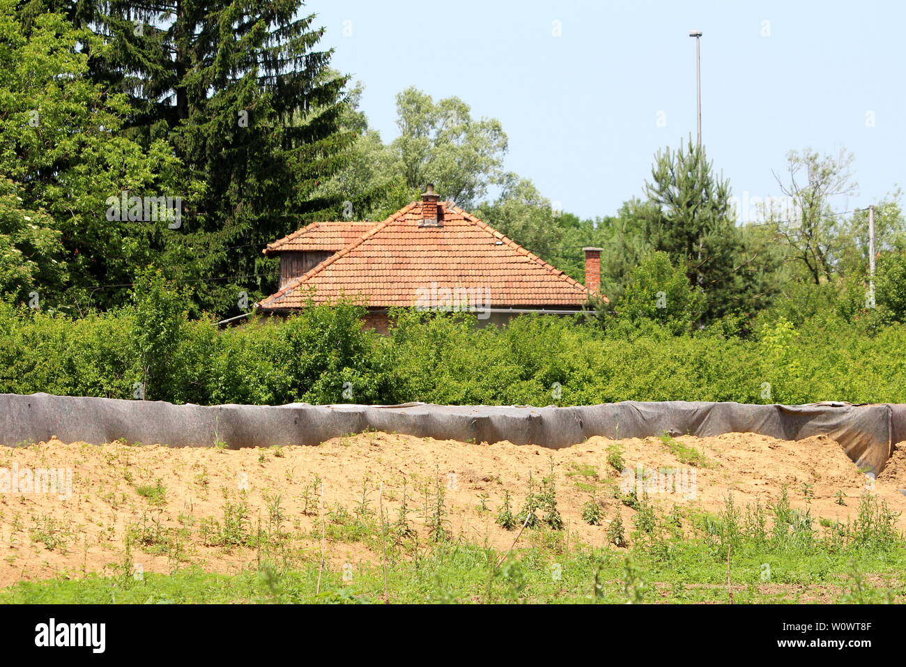 Barely visible family house red roof tiles behind temporary box barriers flood protection covered with dark grey geotextile fabric Stock Photo