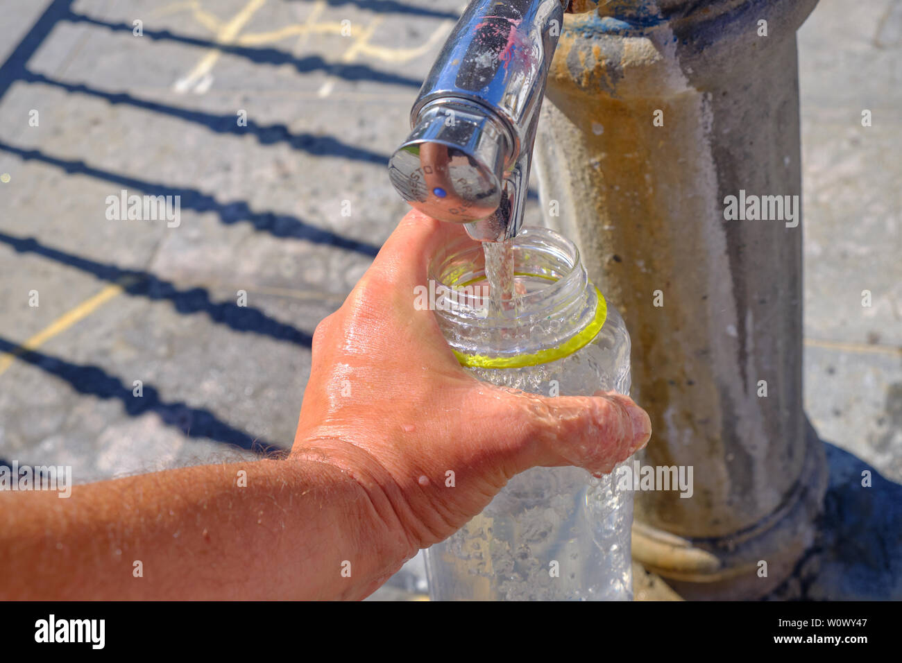 Hand of a hiker filling up his water bottle at a public fountain, to hydrate during the heat wave in Europe. Stock Photo