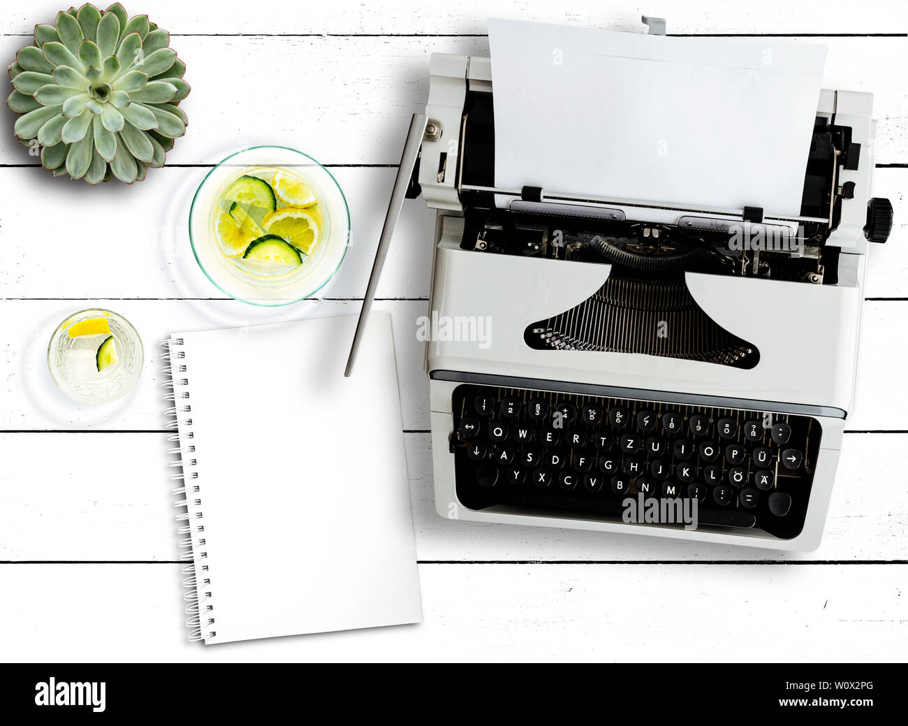 top view of old typewriter, succulent plant, water carafe and notepad on rustic white wooden table Stock Photo