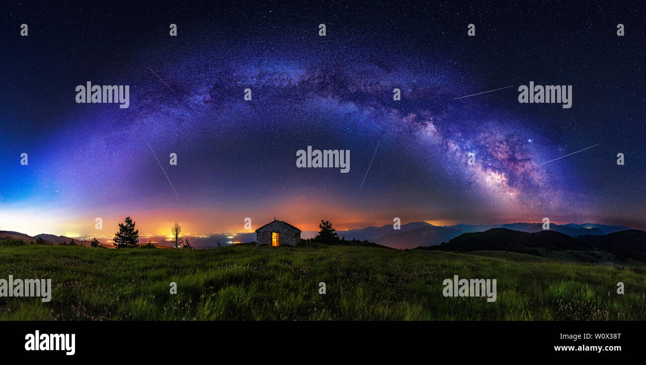 Make a wish - Meteor shower during summer with full arc of milky way. Beautiful Universe. Small chapel in foreground. Space background. Stock Photo
