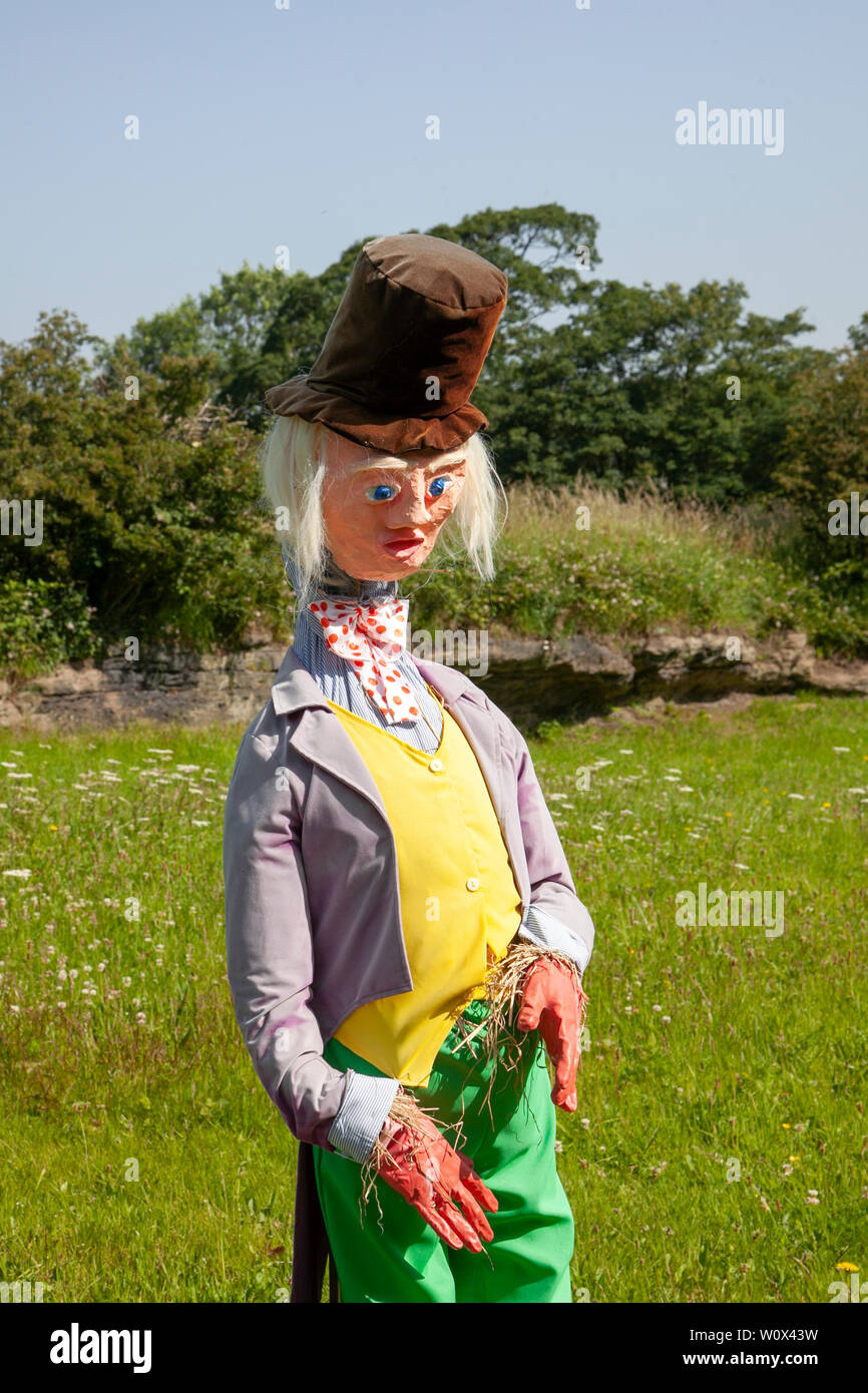 Halsall, Lancashire. 28th June 2019. UK Weather.  Sunny summer sculptures appear over night. Willy Wonka costume black art deco top hat purple tailcoat, yellow waistcoat and bow; Grotesque, quirky, straw filled scarecrows, film characters, caricatures with s line the streets & fields of the rural village of Halsall. Stock Photo