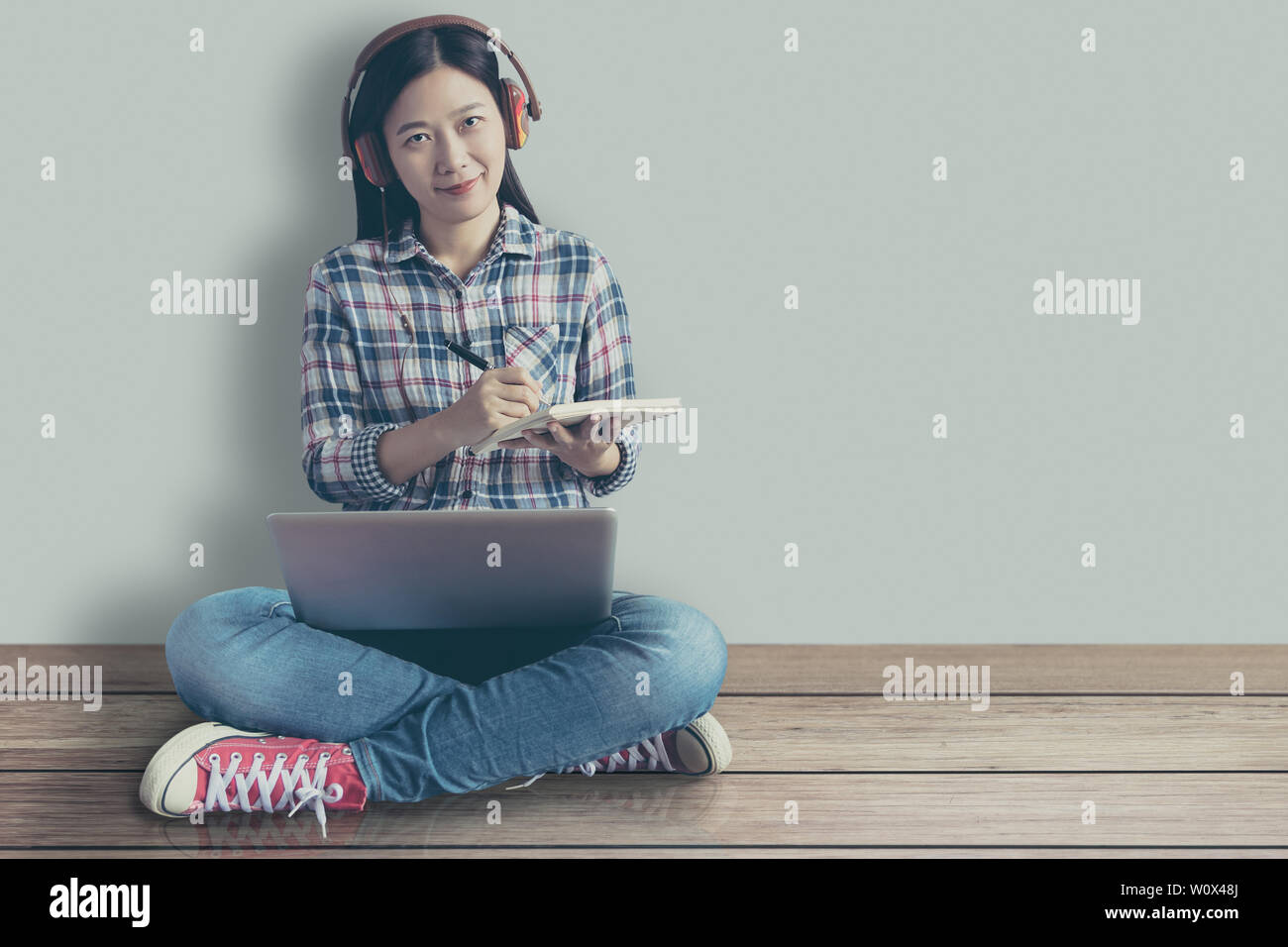female student relaxed sitting on a wooden floor at home and watching training online course and listening it with headphones from compute laptop. onl Stock Photo