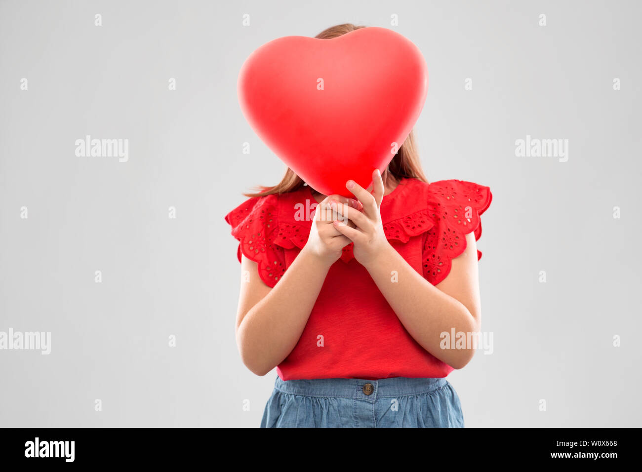 girl hiding behind red heart shaped balloon Stock Photo