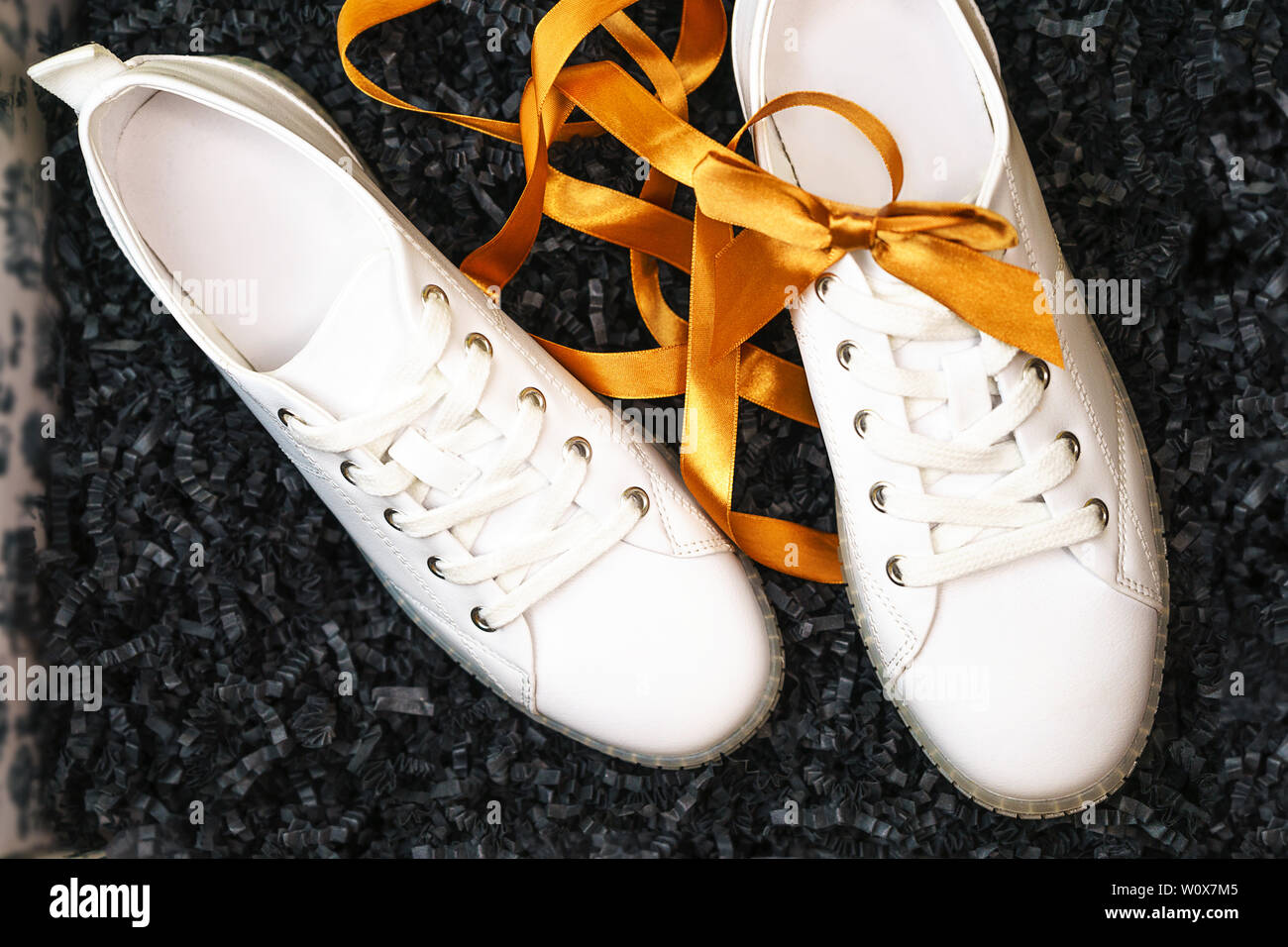white sneakers and yellow bow are lying on textured black box background W0X7M5
