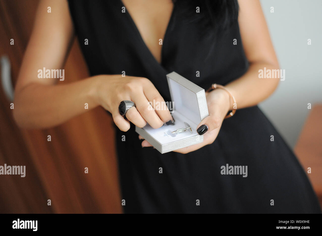 Caucasian woman dressed in an elegant black dress with a black chunky ring and black manicure, holding a small jewelry box with a pair of cuff links Stock Photo