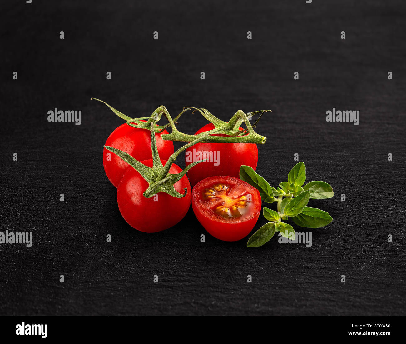 Red cherry tomatoes with green branch on black background Stock Photo