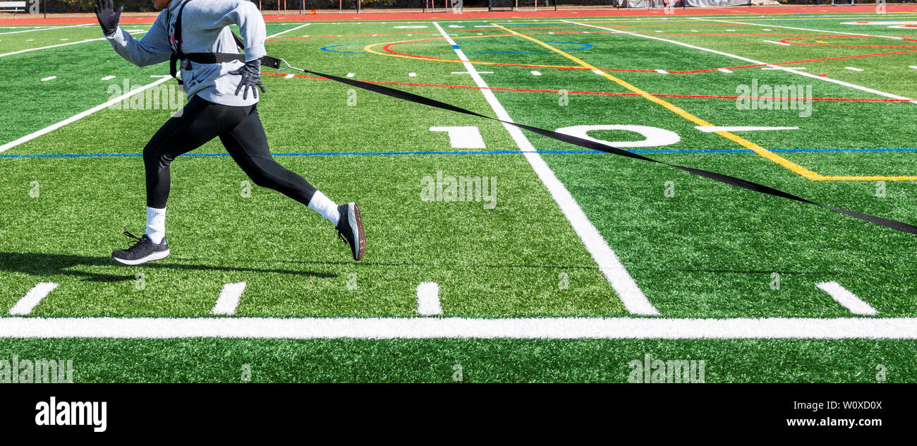 High school track and field runner is pulling a sled with weights across a green turf field