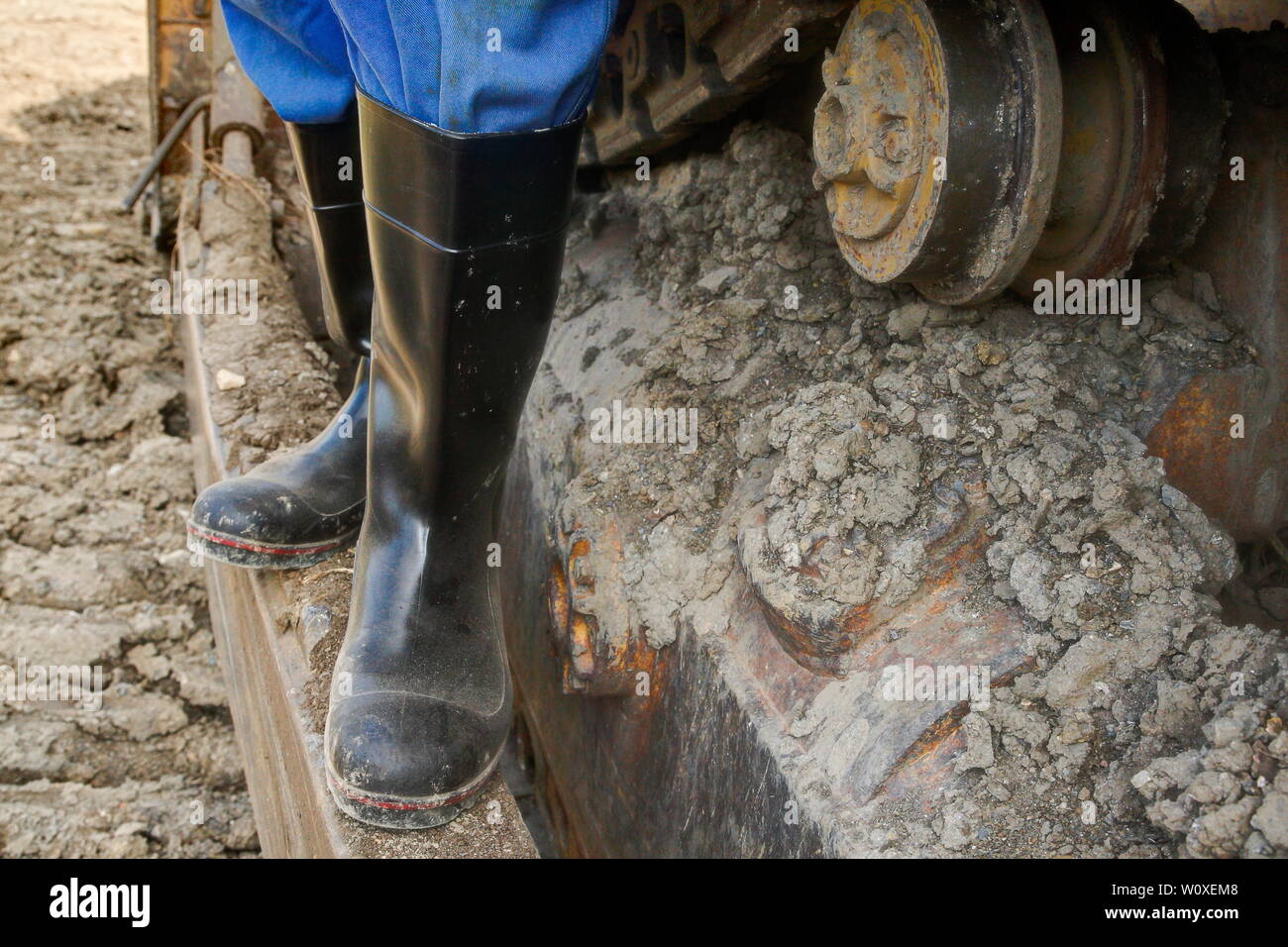 Rubber boots for work use. An excavator driver stands with his dusty rubber boots on the drive chaint of his bulldozer. Stock Photo