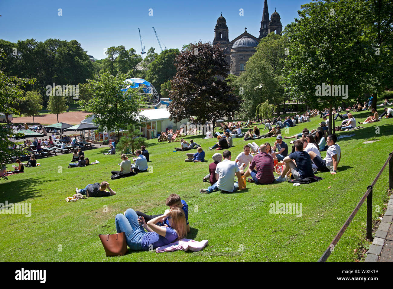 Princes Street Gardens and  Edinburgh, Scotland. 28th June 2019. Full sunshine in the city being enjoyed by office workers and visitors, 14 degrees in the morning with cool  wind increasing to 17 degrees in the afternoon allowing a relaxing lunch hour sunbathe. Stock Photo