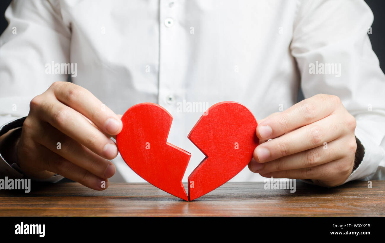 A man collects a broken heart in his hands. Concept of love and relationships. Family psychotherapist services. Reconciliation. Saving the family. Sea Stock Photo