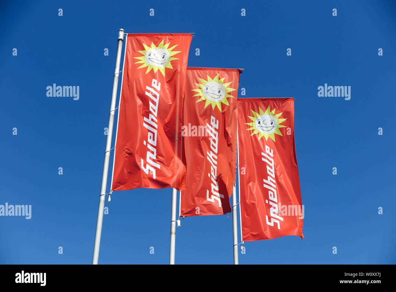 TOENISVORST, GERMANY - JUIN 28. 2019: Close up of red flags against blue sky with sun logo of Merkur Spielothek (german gambling hall chain) Stock Photo