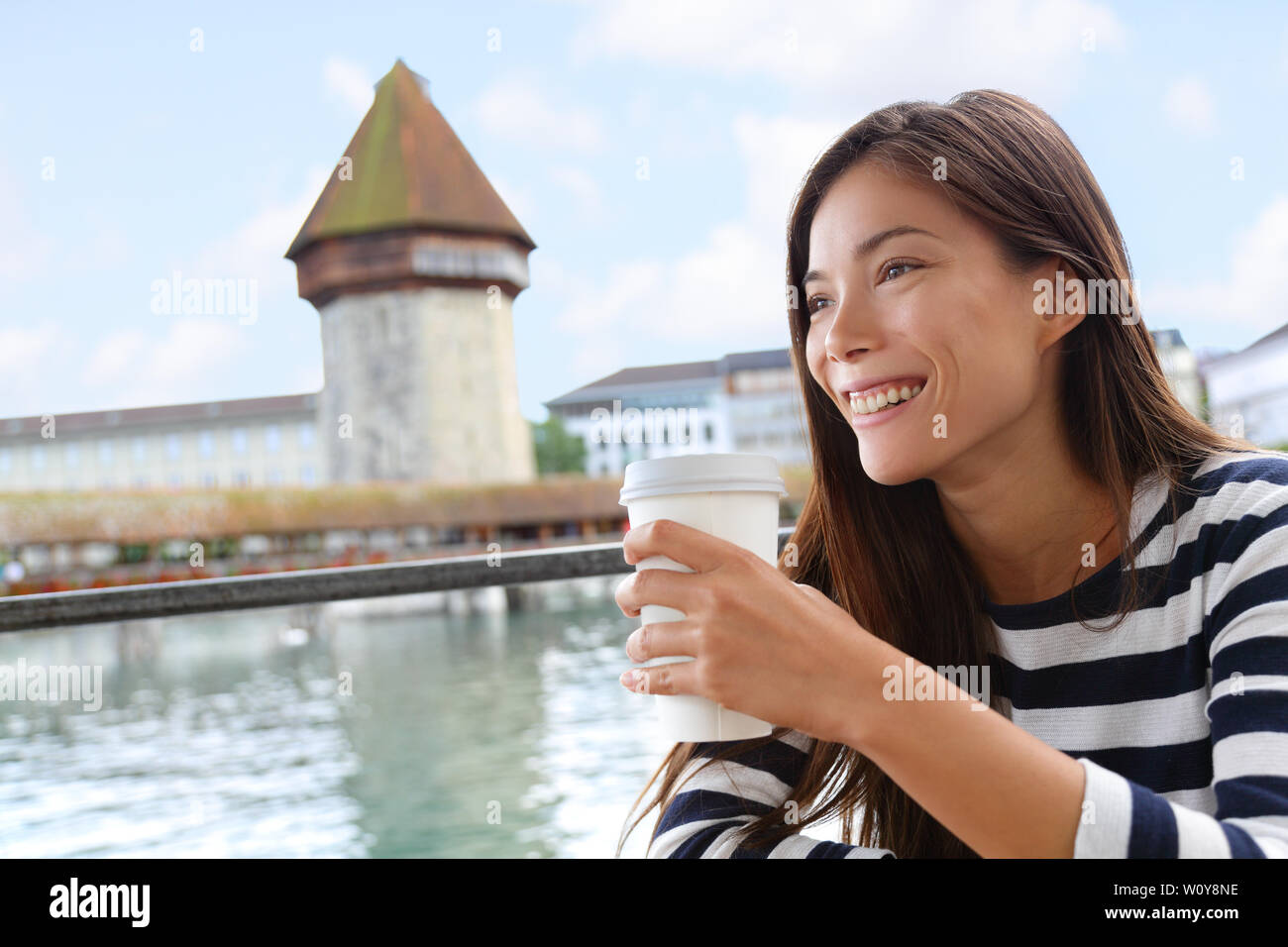 Woman drinking coffee at cafe in Lucerne, Switzerland. Casual girl tourist on travel visiting landmarks tourists attraction Kapellbrucke Chapel Bridge with Wasserturm water tower on Reuss River. Stock Photo