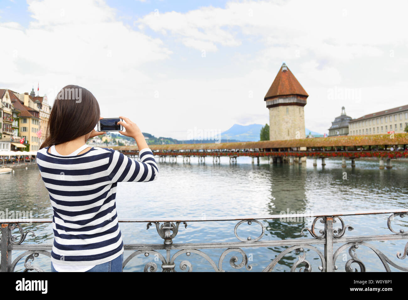 Tourist taking photograph picture with smartphone in Lucerne Switzerland. Travel woman with smart phone by landmark Kapellbrucke Chapel Bridge and Wasserturm water tower, Reuss River Stock Photo