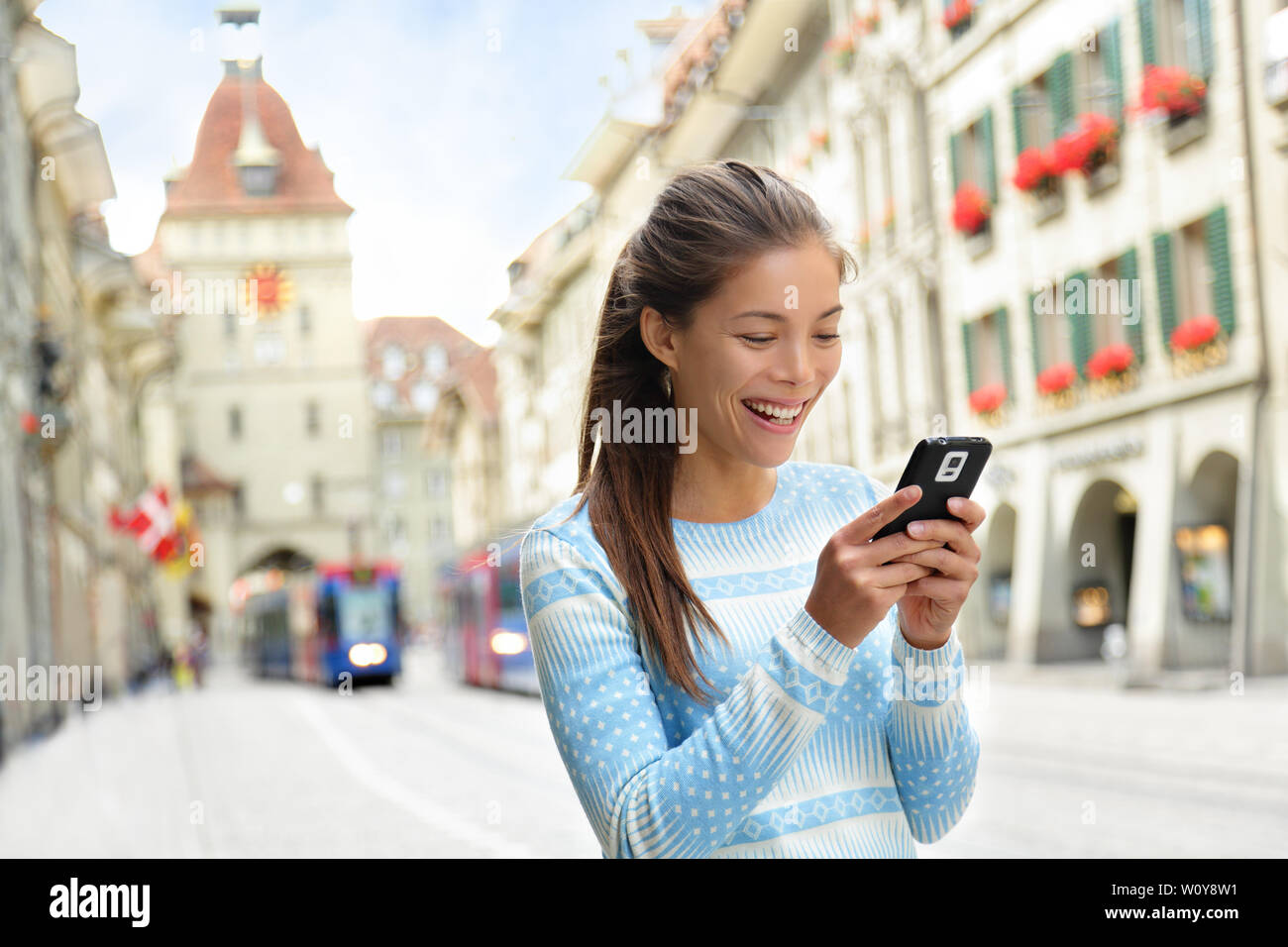 Woman on smart phone walking on Kramgasse, Berne main street in the old city. Young female using smartphone app visiting tourist attractions and landmarks. Stock Photo