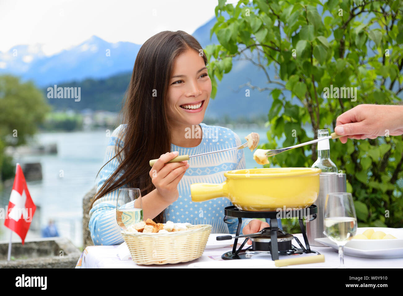 People eating Swiss cheese fondue having dinner in Switzerland by lake in Alps. Woman eating local food having fun on travel in Europe. Romantic couple outdoors in summer. Stock Photo