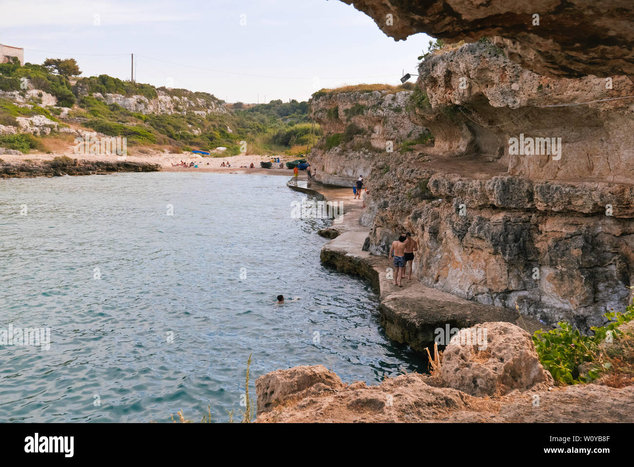 Harbor beach with unrecognizable people far away on the shore who take the relaxing time in the hot afternoon summer of climate mediterranean. Stock Photo