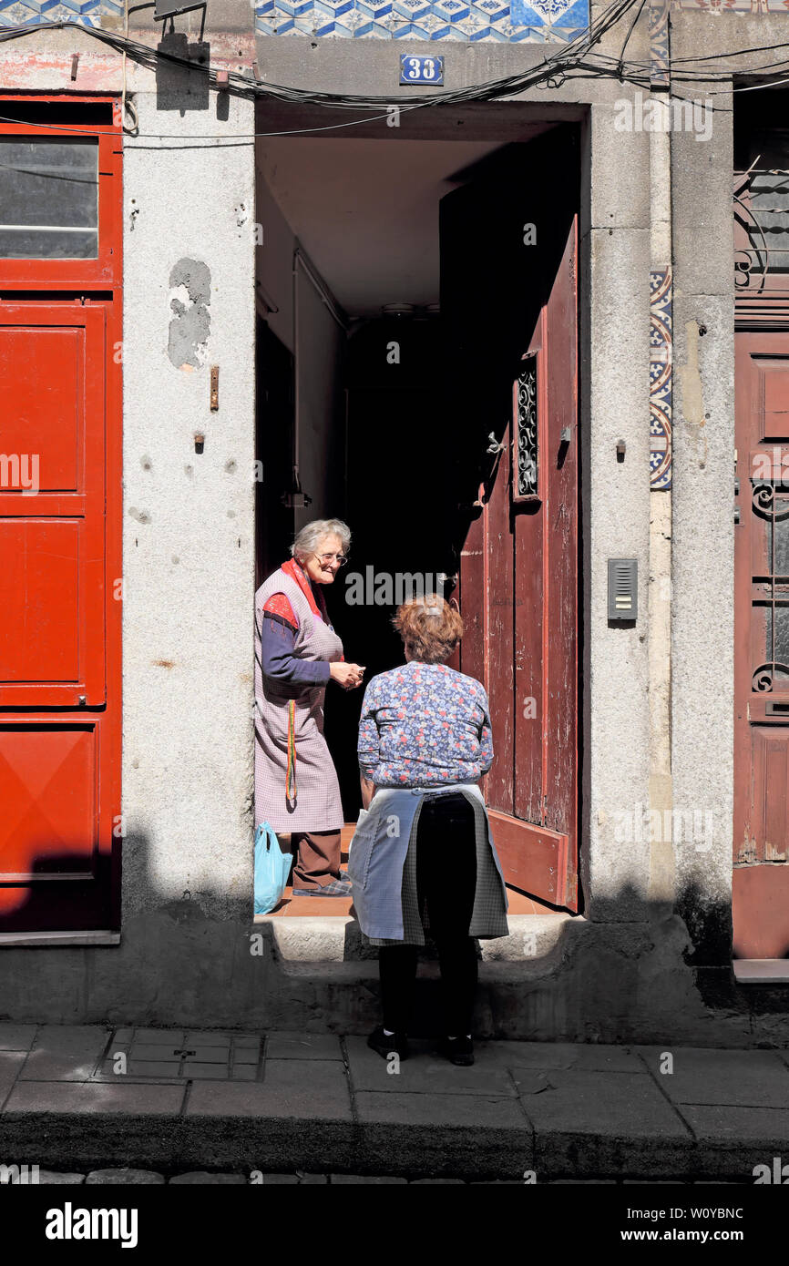 Two older women wearing aprons standing in street on doorstep have a conversation chatting talking Porto Oporto Portugal Europe  KATHY DEWITT Stock Photo