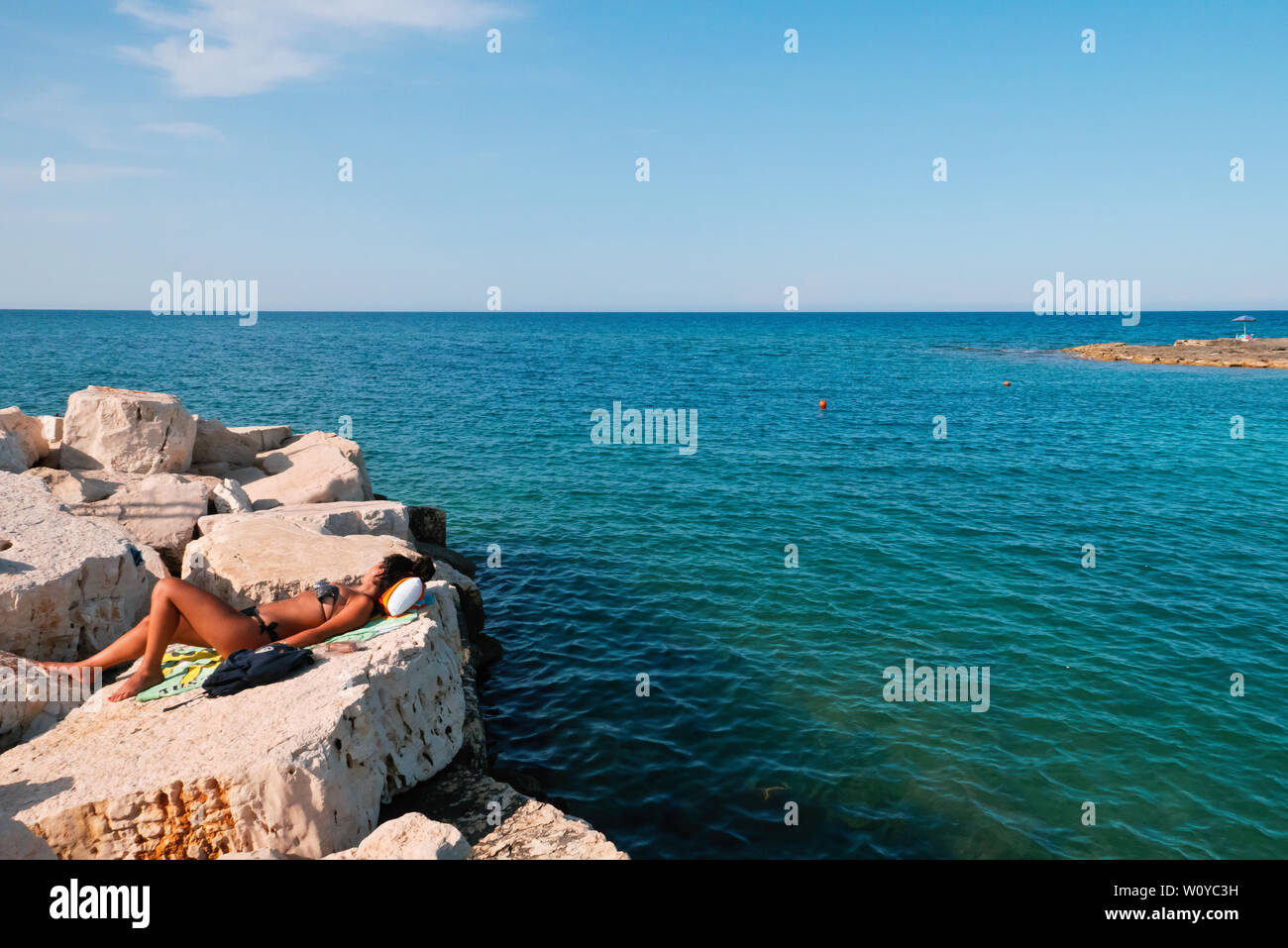 Polignano,Italy,06/21/2019:a girl lying on the beach of Polignano in a sunny summer,who relaxing under hot sun. Stock Photo