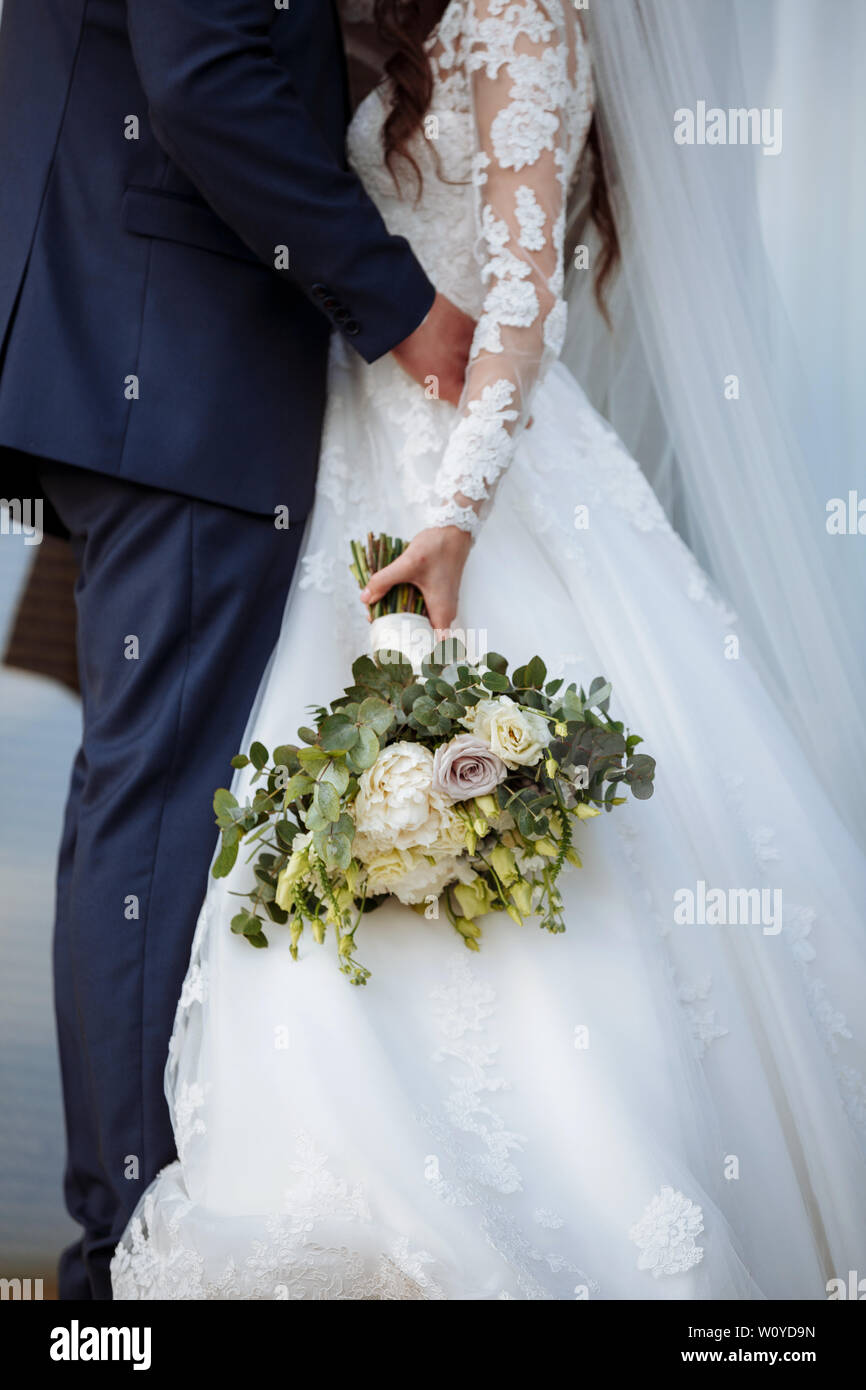 The bride in an elegant wedding dress holds a beautiful bouquet of  different flowers and green leaves. Wedding theme Stock Photo - Alamy