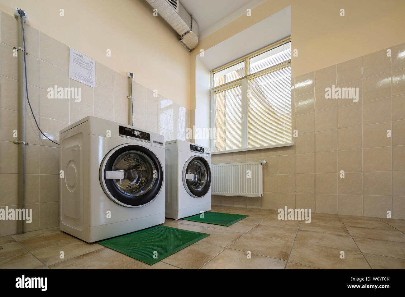 Modern new industrial washing machines on rubber insulation mats in clean light tiled bathroom