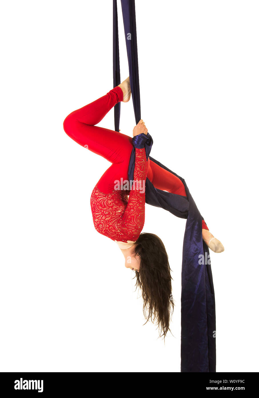 A Young woman with long hair in a red suit performs gymnastic and circus exercises on silk. Studio shooting on white background, isolated image. Stock Photo
