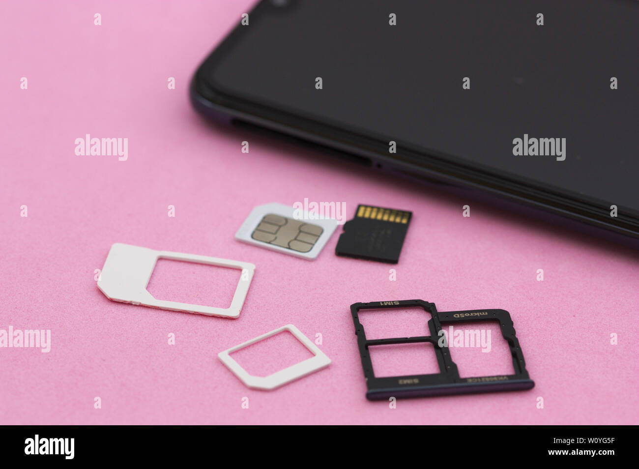 A black smartphone next to the microSD memory cards and the SIM card on a pink background Stock Photo