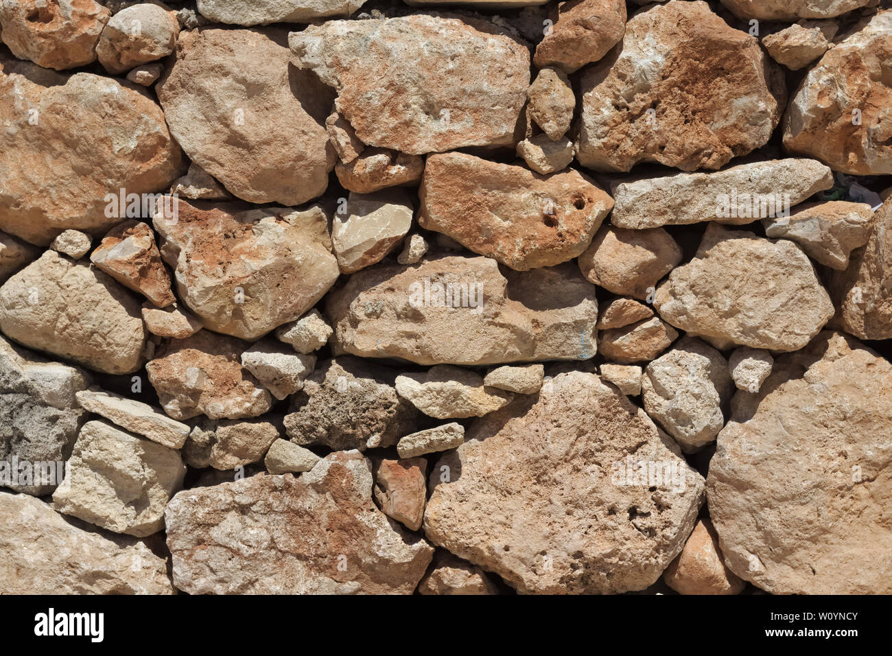 Natural beige stone wall (masonry) created by stacking stones on top of each other with varying stone sizes. Stock Photo