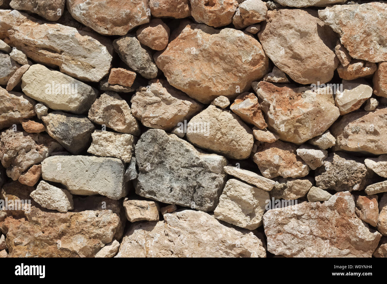 Natural beige stone wall (masonry) created by stacking stones on top of each other with varying stone sizes. Stock Photo
