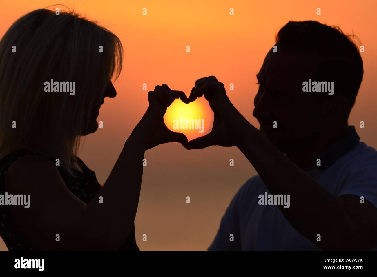 Aberystwyth, Wales, UK. 28th June 2019. UK weather: A couple frame the sunset between their fingers in the shape of a heart  in Aberystwyth on a sweltering summer  evening after a day of unbroken blue skies and hot sunshine. The country is heading towards the hottest day of the year so far as a plume of scorching hot air drifts in from the continent.  Photo credit Keith Morris / Alamy Live News Stock Photo
