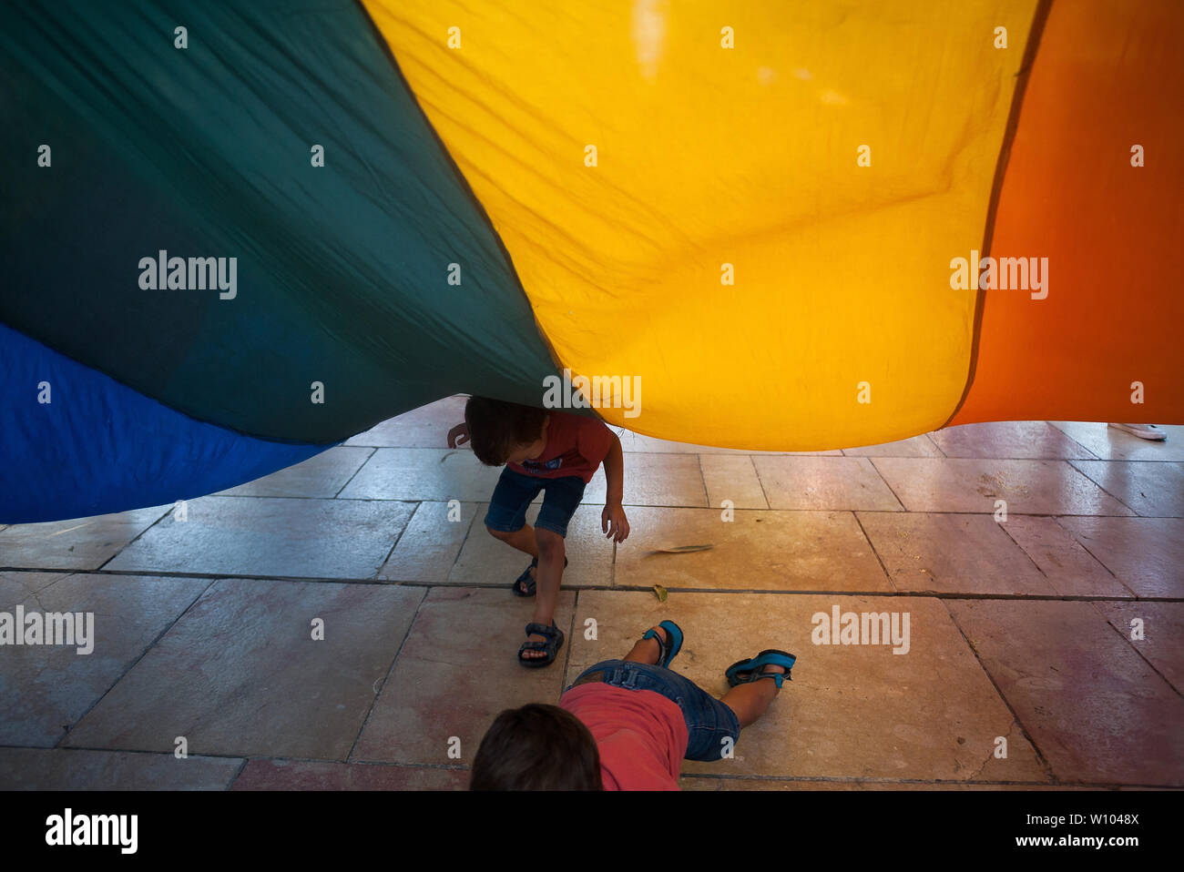 Two boys play under a large pride flag during a demonstration to celebrate the International Pride LGTBI Day 2019, organized by Andalusia Rainbow Federation.Thousands of people around the world take part on the Pride LGTBI, marked the anniversary of 50 years of Stonewall riot which commemorated the fight of gays, lesbians, transgender, bisexuals and intersexual during the first demonstrations in US in favour of their rights. Stock Photo